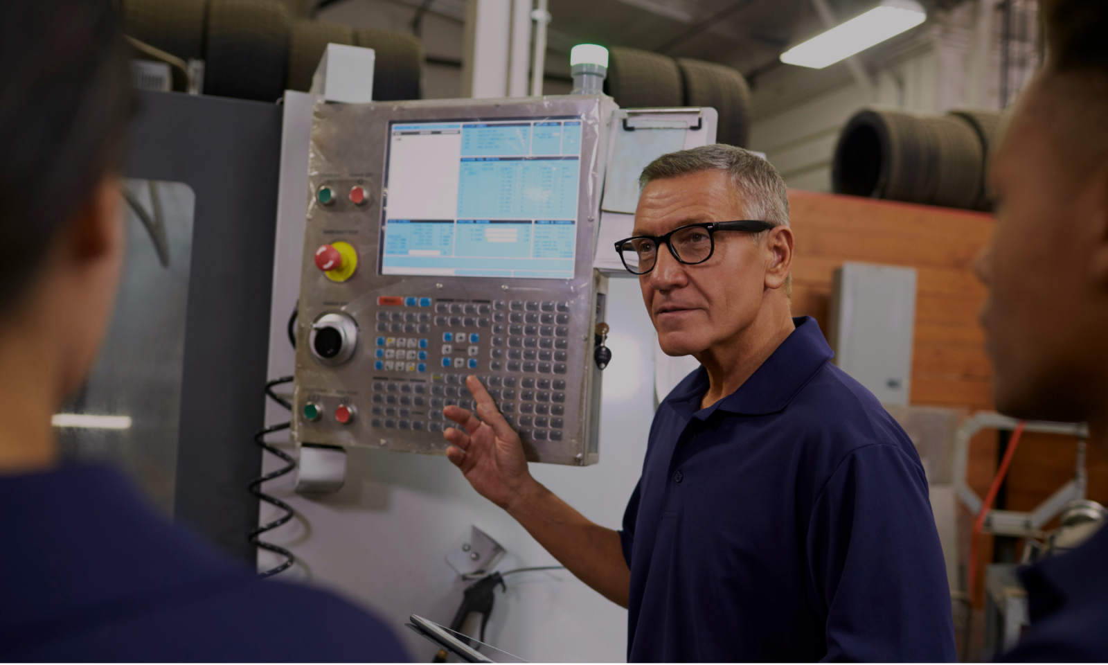 An operator explaining a CNC machine control panel to colleagues on a shop floor.