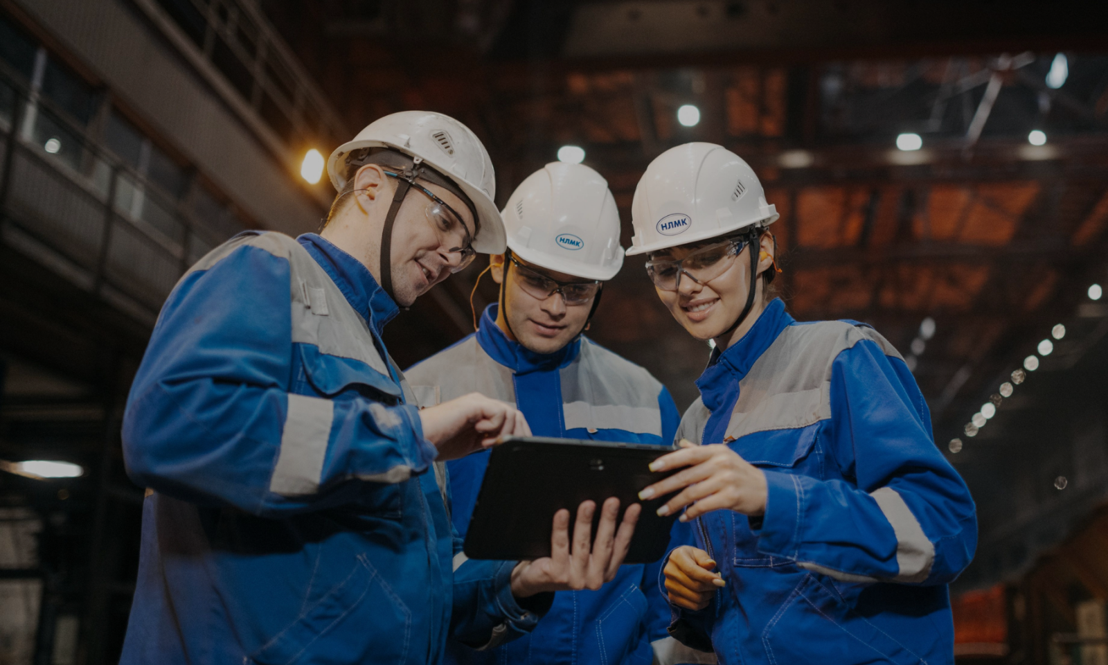 Three manufacturing workers in hard hats looking at a tablet on the shop floor