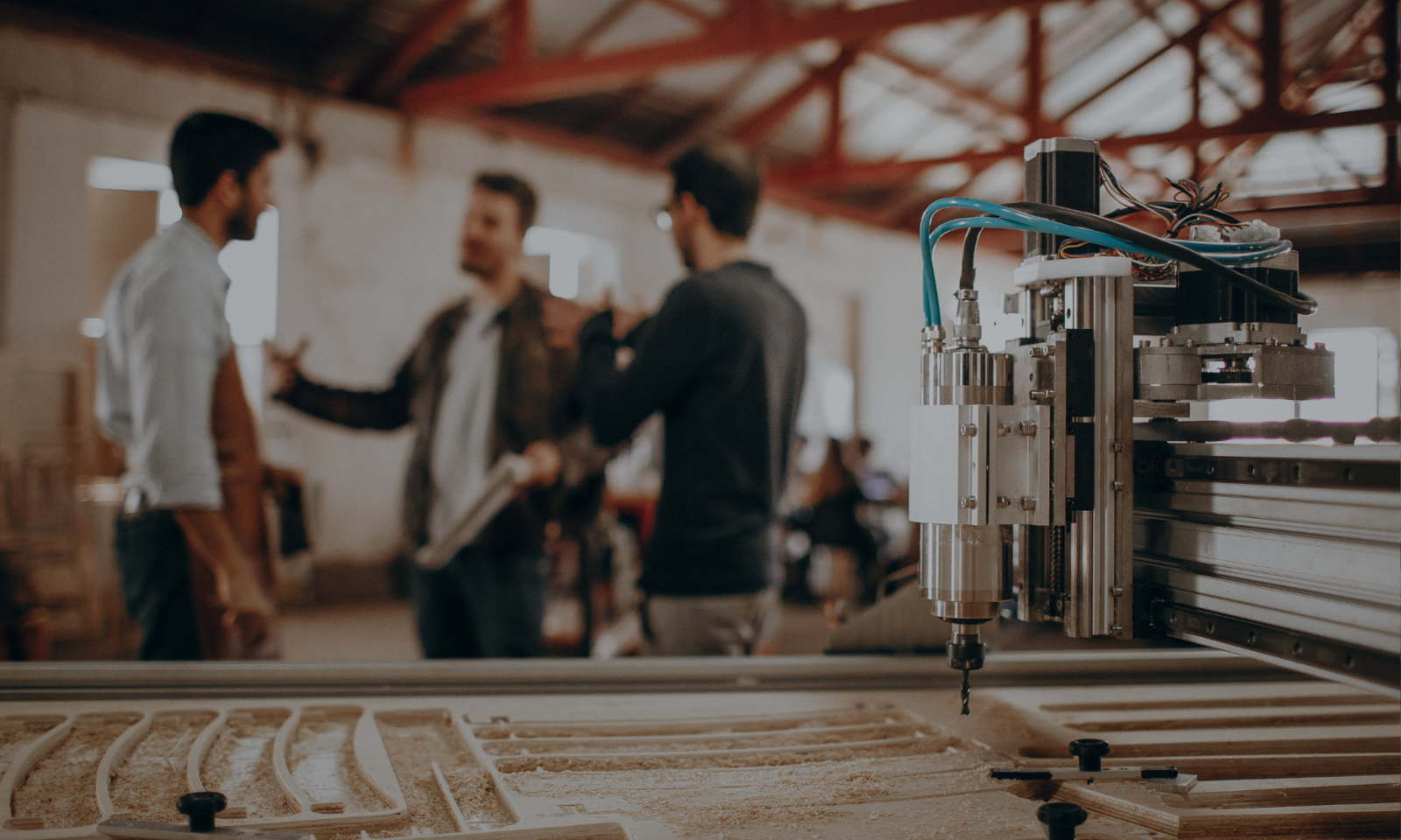 Alt text: Three people having a discussion in a machine shop with a CNC machine in the foreground