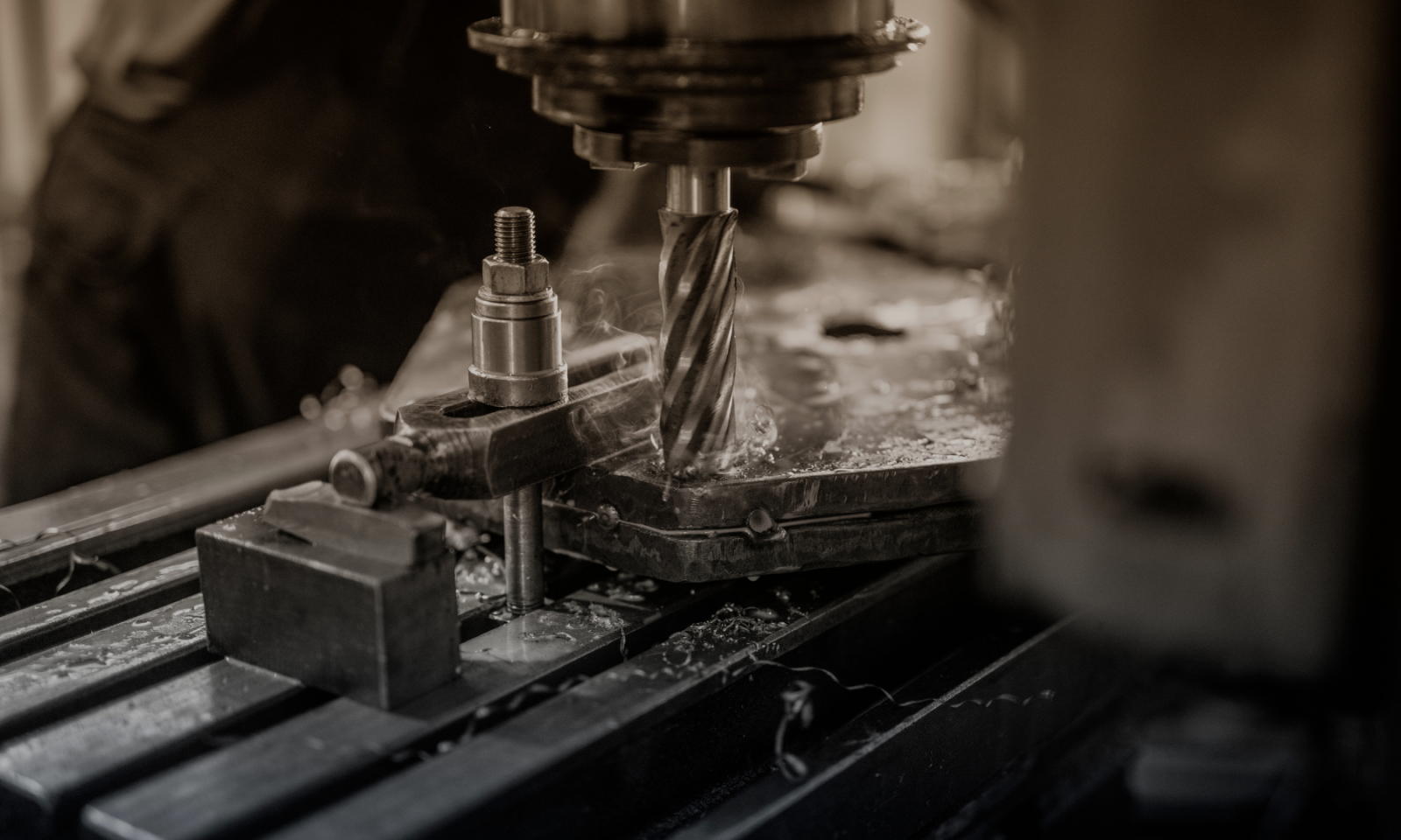 End mill cutting into a metal workpiece clamped on a CNC machine table, with coolant vapor rising and chips scattered across the surface.