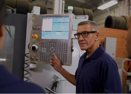 An operator explaining a CNC machine control panel to colleagues on a shop floor.