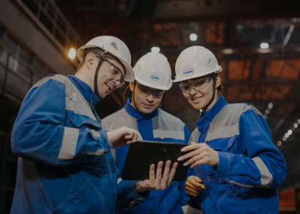 Three manufacturing workers in hard hats looking at a tablet on the shop floor