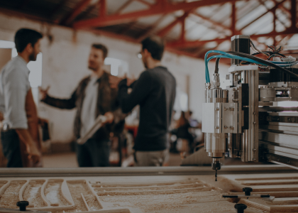 Alt text: Three people having a discussion in a machine shop with a CNC machine in the foreground