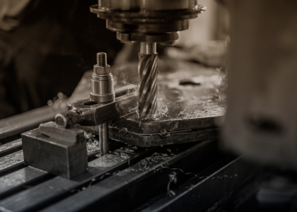 End mill cutting into a metal workpiece clamped on a CNC machine table, with coolant vapor rising and chips scattered across the surface.