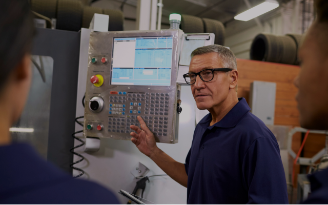 An operator explaining a CNC machine control panel to colleagues on a shop floor.