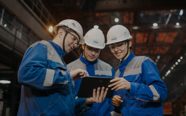 Three manufacturing workers in hard hats looking at a tablet on the shop floor