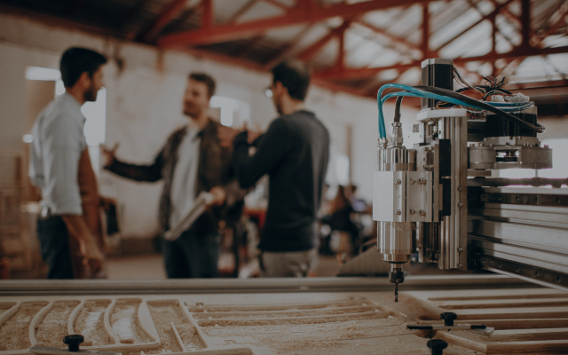 Alt text: Three people having a discussion in a machine shop with a CNC machine in the foreground