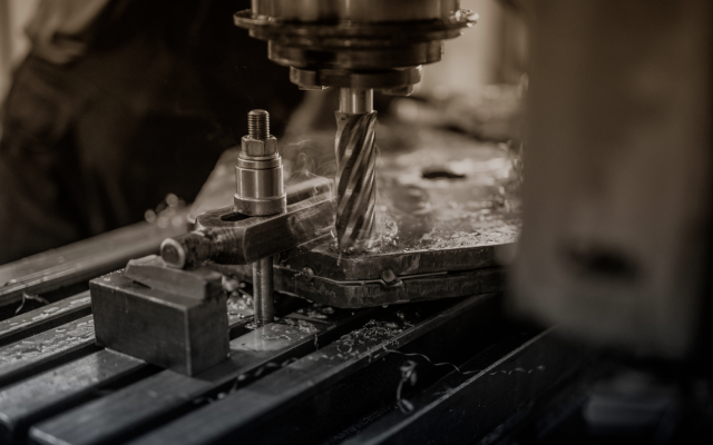 End mill cutting into a metal workpiece clamped on a CNC machine table, with coolant vapor rising and chips scattered across the surface.