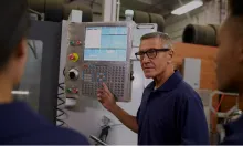 An operator explaining a CNC machine control panel to colleagues on a shop floor.