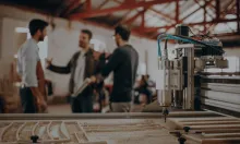 Alt text: Three people having a discussion in a machine shop with a CNC machine in the foreground